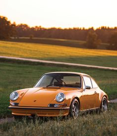 an orange car parked on the side of a dirt road in front of a field