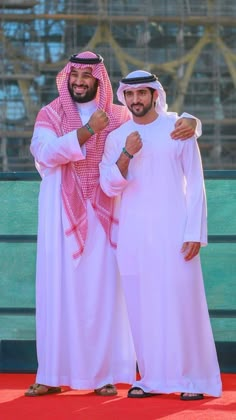 two men standing next to each other in front of a green wall and red carpet