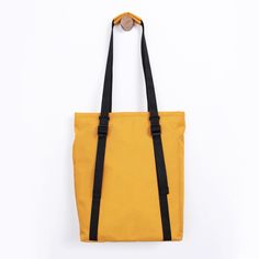 a yellow tote bag with black straps hanging from the side on a white background