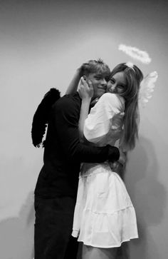 a man and woman hugging each other in front of a wall with angel wings on it