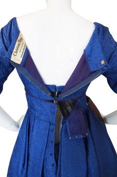 the back of a blue dress with purple linings and an attached belt, on a mannequin's head