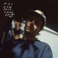 a man wearing a hat standing in front of a white wall with writing on it