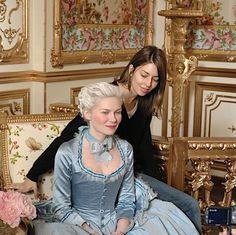 two women are sitting on a couch and one is wearing a blue dress