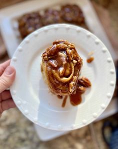 a person holding a white plate with some food on it and caramel sauce drizzled over the top