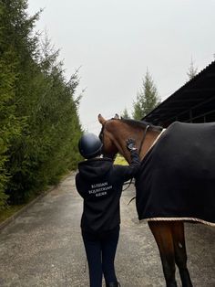 a woman standing next to a brown horse wearing a black cover on it's face