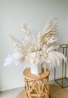 a vase filled with white flowers sitting on top of a wooden table next to a plant