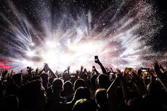 a crowd of people at a concert with their hands in the air and fireworks coming from them