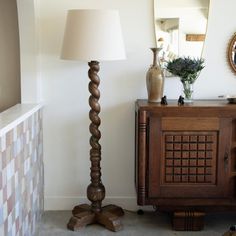 a lamp is next to a wooden cabinet and mirror in a room with tile flooring