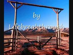 a wooden gate in the middle of a dirt field with mountains in the back ground