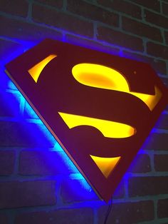 the superman symbol is lit up in blue and yellow colors on a brick wall with a neon light underneath it