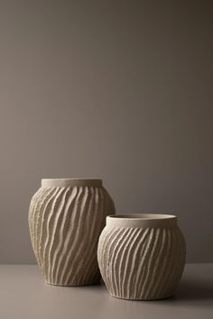 two white vases sitting next to each other on top of a table in front of a gray wall