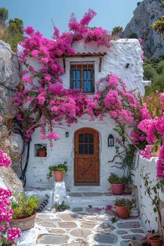 a white house with pink flowers growing on it's windows and door, surrounded by stone steps