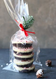 three cookies wrapped in plastic and tied with a red ribbon, sitting next to pine cones