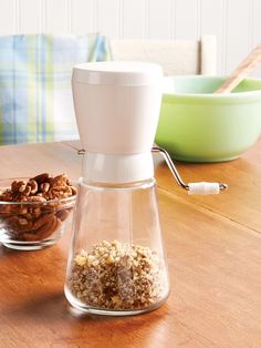 a glass carafe filled with nuts sitting on top of a wooden table next to two bowls