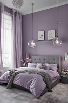 a bedroom decorated in purple and grey with two lamps hanging from the ceiling above the bed