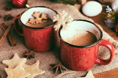 two red mugs filled with hot chocolate on top of a table next to christmas decorations