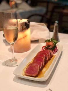 a white plate topped with meat next to a glass of wine