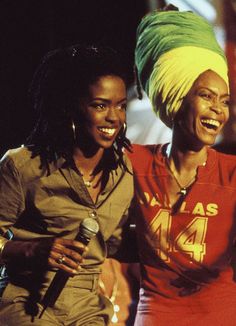 two women standing next to each other with one holding a microphone and the other smiling