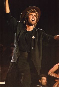 a man wearing a hat and holding his arms in the air while standing on stage