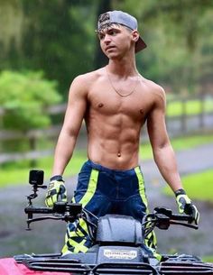 a shirtless man standing on top of a red four - wheeler in the rain