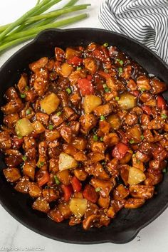 a skillet filled with chicken and vegetables on top of a white table next to green onions