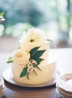 a wedding cake with white flowers and greenery sits on a table next to plates