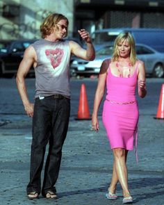 a woman in a pink dress walking next to a man wearing a gray t - shirt