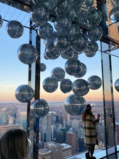 a person standing on top of a tall building with lots of glass balls hanging from the ceiling