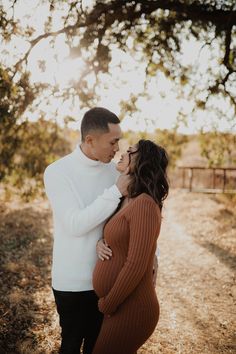 a man and woman standing next to each other on a dirt road under a tree