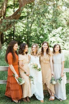 a group of women standing next to each other in front of a wooden fence holding bouquets