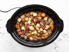 a crock pot filled with meat and vegetables on a marble counter top, ready to be cooked