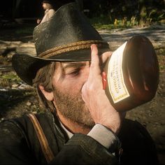 a man wearing a hat and holding a bottle in front of his face while looking through the lens