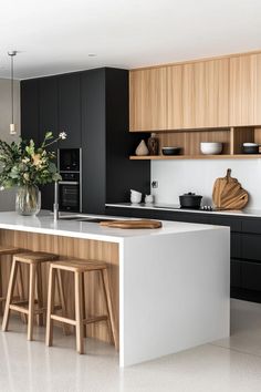 a kitchen with black cabinets and white countertops has stools in front of the island