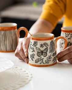 two coffee mugs are being held by someone's hands at a table with plates on it