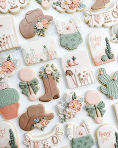 many decorated cookies are arranged on a white tablecloth with pink and green accents, such as cowboy boots, hats, flowers, and cactuses