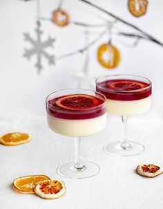 two glasses filled with red wine and orange slices on a white tablecloth next to an ornament