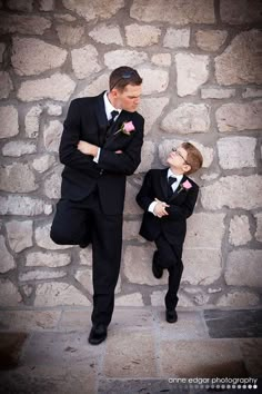 a man in a suit and tie standing next to a little boy wearing a tuxedo