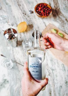 someone is holding a bottle of vodka on a table with other bottles and glasses in the background