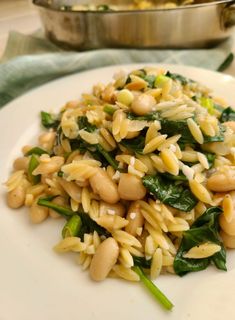 a white plate topped with pasta and greens next to a pot of broccoli