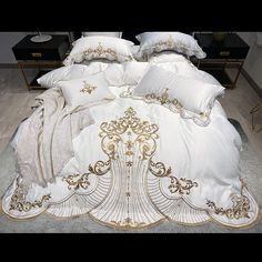 a bed with white and gold comforters on top of it in a room next to a table