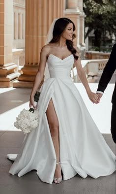 a bride and groom holding hands walking down the street