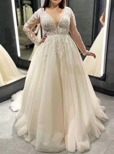 a woman standing in front of a mirror wearing a wedding dress with long sleeves and beading