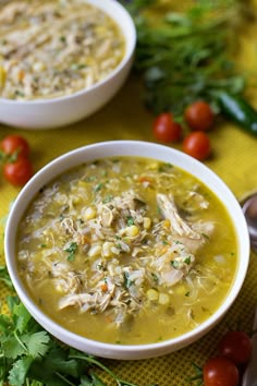 two bowls of chicken and corn soup on a yellow table cloth with tomatoes, cilantro, and parsley