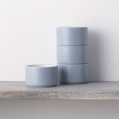 three grey cups sitting on top of a wooden shelf next to each other in front of a white wall