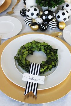 a table set with white plates, black and gold decorations and greenery on it