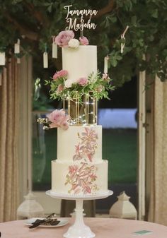 a wedding cake with pink flowers and greenery on top sits on a round table