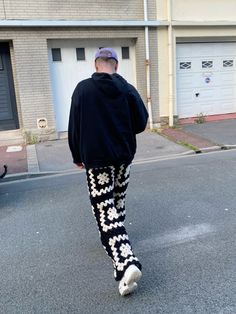 a man is walking down the street in patterned pants and a black hoodie with white flowers on it