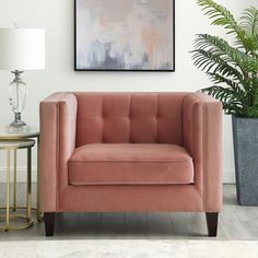 a pink chair sitting next to a table with a lamp and potted plant on it