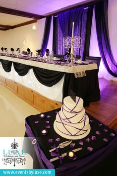 a wedding cake is on top of a table with purple and black decor at the end