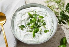 a bowl filled with white dip surrounded by herbs